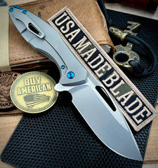 Koenig Arius Patterned Ti Stonewashed M390 Blade with Polished Flats and Blue Ti Hardware AR11211221
