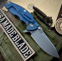 Hinderer Jurassic Hollow Ground Slicer Black G10 Battle Blue Ti Magnacut Working Finish Blade